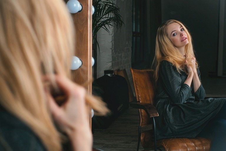 woman sitting in brown leather chair looking at herself in mirror