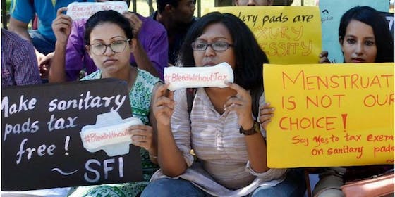 three women with signs make sanitary pads tax free